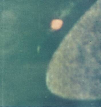 Grainy image of a curved planetary edge with a small orange oval object nearby