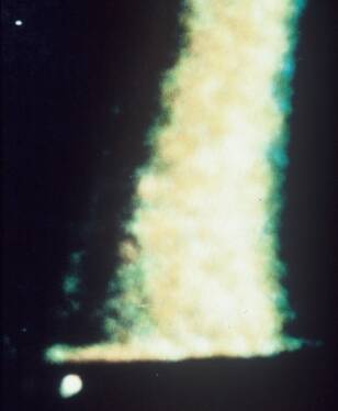 Grainy glowing column of light with a small bright dot below it against black space